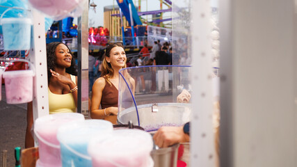 Multiethnic women buying cotton candy at fair.