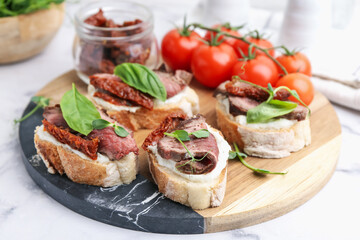 Bruschettas with roast beef, cream cheese, basil, sun-dried tomatoes and fresh vegetables on white marble table, closeup