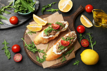 Delicious bruschettas with tuna, tomatoes, arugula, lemons and oil on grey table, flat lay