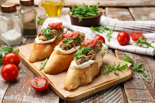 Delicious bruschettas with tuna, cream cheese and tomatoes on wooden table, closeup