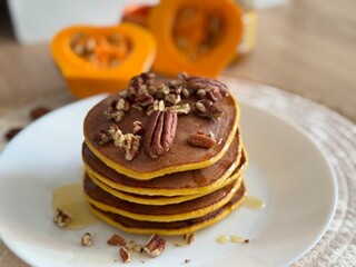 pancakes with chocolate Stack of homemade pumpkin pancakes topped with chocolate cream and pecans. Autumn breakfast concept with fresh pumpkin in the background.