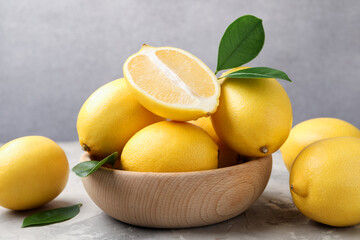 Whole, cut lemons with green leaves and bowl on grey textured table, closeup
