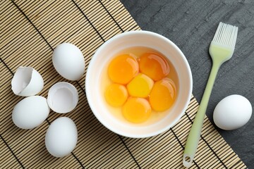 Raw eggs, yolks and brush on black table, flat lay