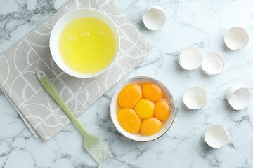 Egg whites, yolks and brush on white marble table, flat lay