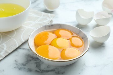 Egg yolks and whites in bowls on white marble table, closeup