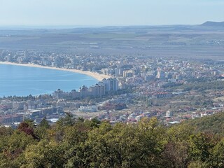 Panoramic view of a coastal city with modern buildings and a long beach curving along the bay. Bright daylight and blue sea horizon. Urban and nature harmony.