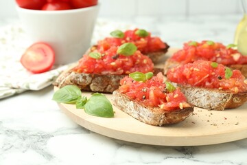 Tasty bruschettas with tomatoes and basil on white marble table, closeup