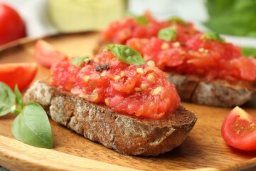 Tasty bruschettas with tomatoes and basil on wooden board, closeup