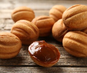 Tasty nut shaped cookies with boiled condensed milk on wooden table, closeup