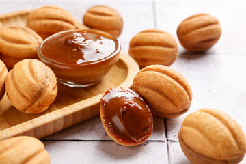 Delicious nut shaped cookies with boiled condensed milk on light tiled table, closeup