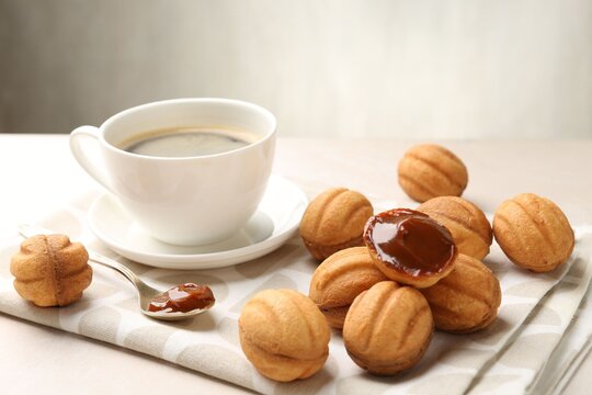 Delicious nut shaped cookies with boiled condensed milk and coffee on light table, closeup