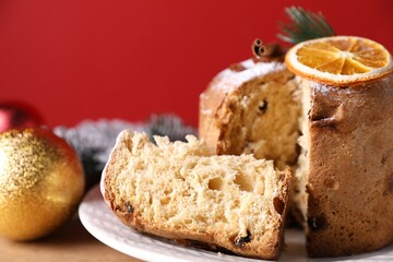 Christmas food. Delicious Panettone cake and festive decor on beige table against red background, closeup