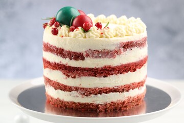 Delicious sponge cake with Christmas decor and red currants on stand against blurred grey background, closeup