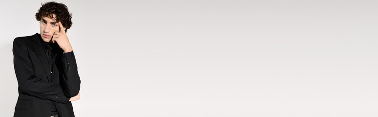 Stylish young man poses thoughtfully in modern attire against a minimalist background