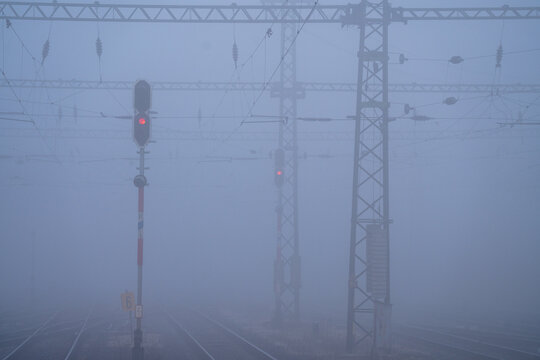 Budapest, Hungary - December 19, 2024: Thick fog covers the railway tracks at a station, with red signals glowing faintly through the misty morning air.