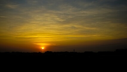 Vivid golden sunset sky over dark silhouette horizon and glowing sun.