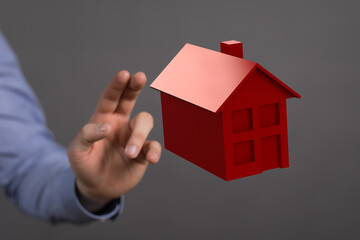 A hand reaching towards a small red house. Represents real estate, property, homeownership, and the dream of owning a home. Perfect for finance