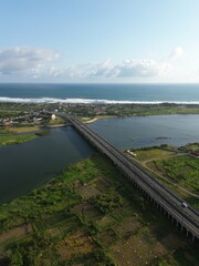 Special Region of Yogyakarta, Indonesia - October 15, 2025 : Aerial View Of Coastal Town With Bridge Over Water And Green Fields