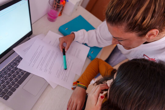 Mother helping teenage girl with homework, studying and learning together at home, looking at papers and laptop - Powered by Adobe