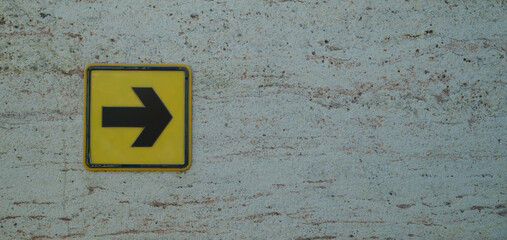 Yellow navigation arrow sign on textured stone wall