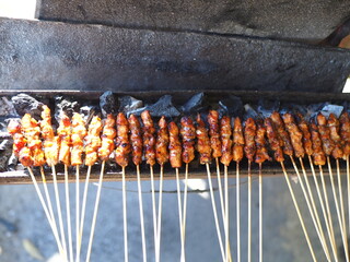 Indonesian satay skewers grilling over hot charcoal, with smoke rising. A classic Southeast Asian street food of seasoned, skewered meat being cooked to perfection.
