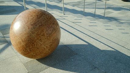 Beige marble sphere on concrete stairs with strong angular shadows