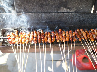 Indonesian satay skewers grilling over hot charcoal, with smoke rising. A classic Southeast Asian...