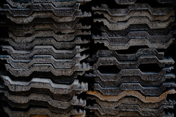 Close-up view of stacked old concrete roofing tiles arranged in rows. The weathered surface and rough texture show signs of age and use, creating a pattern of repeating shapes and earthy tones. Perfec