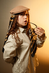 Stylish woman wearing flat cap and scarf holding glasses