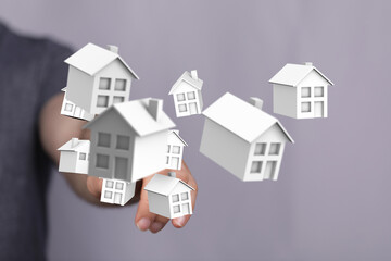 Person holding miniature houses, a visual representation of housing, property investment, real estate market, and dream home ownership concept.