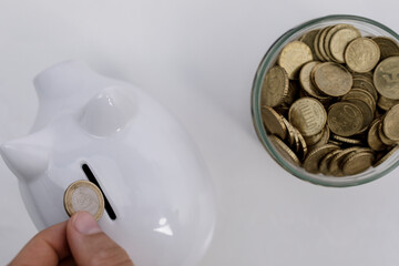 A hand placing a coin into a piggy bank, with a jar full of coins, representing savings, investment, and financial planning. Ideal for finance,