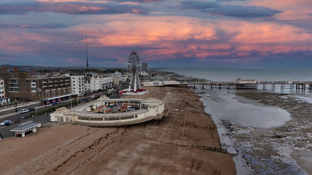 Aerial view of the Worthing Pier extending into the sea, with the Ferris wheel standing tall against the dramatic, colorful sunset sky, Worthing, England, United Kingdom.