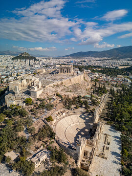 Aerial view of the ancient Acropolis, the Theater of Dionysus, and the distant Mount Lycabettus under a bright blue sky, Athens, Greece.