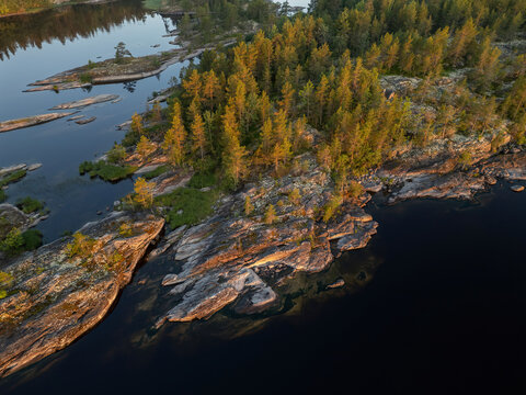 Aerial view of rocky, sun-kissed islands crowned with vibrant green forests, standing resiliently against the dark waters of Lake Ladoga, Sortavala, Russia.