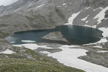 Mountain lake in summer among the mountains of Arkhyz on the slopes of melting glaciers, snow, ice and clouds envelop the mountains, a lot of stones and boulders