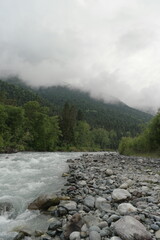 A stormy mountain river flows between rocks, boulders and cliffs in Arkhyz against a backdrop of...