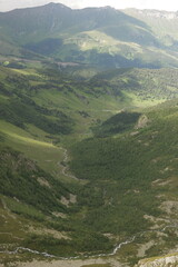 Fototapeta premium View of the valley between the Arkhyz mountains and the mountain river meanders between a hills. The slopes are overgrown with trees, shrubs and grass, covered with snow and melting glaciers
