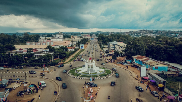 Aerial view of a bustling roundabout with the prominent 'Plateau State' monument amidst a cityscape under a dramatic sky, Jos, Plateau State, Nigeria.