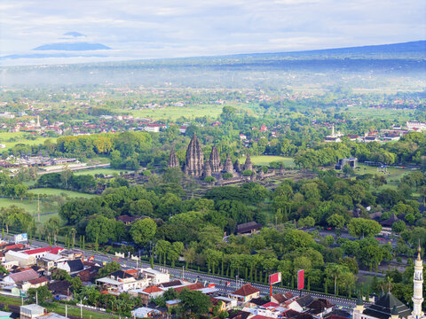 Aerial view of ancient temples rising amidst a sea of lush green trees, with distant mountains painting the horizon, Yogyakarta, Daerah Istimewa Yogyakarta, Indonesia.