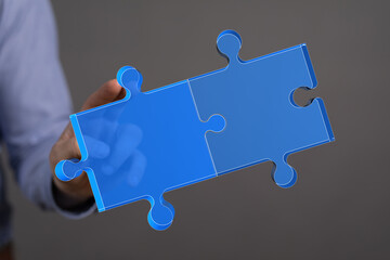 A person's hand holding two connected puzzle pieces. Representing teamwork, solutions,...