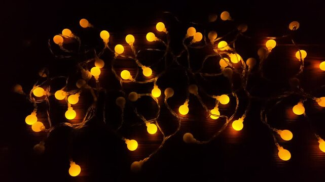 Warm glow of decorative garland lights on dark wood background radiates holiday cheer, inviting joy and happiness for Christmas and New Year celebrations