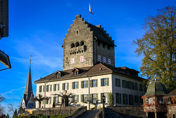 Historic castle in Uster, Zürcher Oberland, with stepped gables and Swiss flag, standing beside a church tower under a clear blue sky