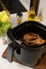 Air fryer basket with cooked chicken drumsticks, vegetables and spices on white marble countertop, closeup