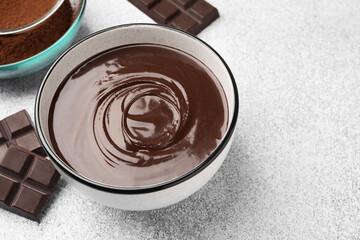 Melted chocolate in bowl, pieces and cocoa powder on light grey table, closeup. Space for text