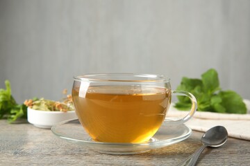 Tasty tea in glass cup and teaspoon on wooden table against grey background, closeup