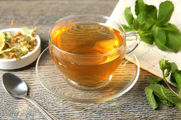 Tasty tea in glass cup, linden, mint and teaspoon on wooden table, closeup