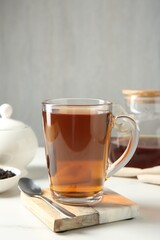 Tasty tea in glass cup and teaspoon on white table against grey background, closeup