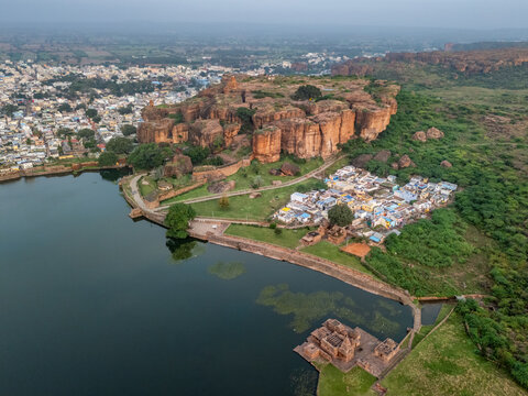 Aerial view of ancient red sandstone cliffs meeting the tranquil waters of Agastya Lake, where history and nature converge in a stunning landscape, Badami, Karnataka, India.