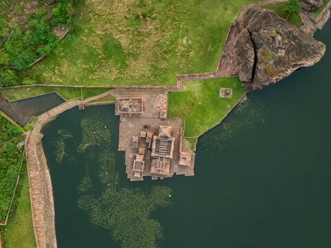 Aerial view of Bhutanatha Temple complex reflecting in the still, dark waters of the lake, framed by rugged cliffs and verdant greenery, Badami, Karnataka, India.