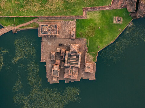 Aerial view of the Bhutanatha temple complex with its reddish-brown sandstone structures reflected in the serene waters of the lake, Badami, Karnataka, India.